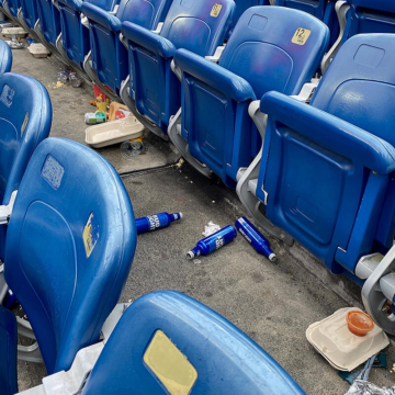 Trash scattered across seating section at Gillette Stadium after game day, with an expansion joint visible along the concrete walkway between rows of seats.