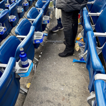 Expansion joint running through stadium stair treads and risers with game day trash scattered on and around the joint.