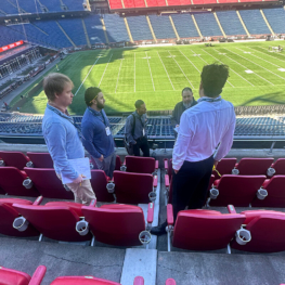 Sika Emseal team members comparing notes from a stadium expansion joint walkthrough with the football field and seating bowl visible in the background at Gillette Stadium.