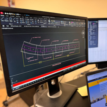A close‑up view of a computer monitor showing an AutoCAD drawing of a curved expansion joint and cover plate assembly. The drawing includes dimensioning, plate alignment, and bolt layout details for the MTA station deck.