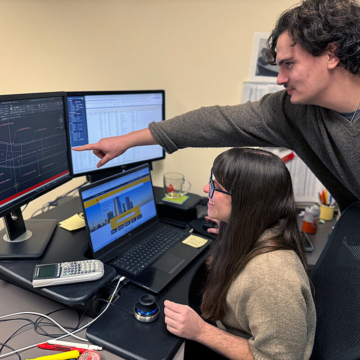 Two engineering team members collaborate at a workstation, reviewing a detailed AutoCAD model of the curved expansion joint. One person points to design elements on the screen while discussing adjustments based on field measurements.